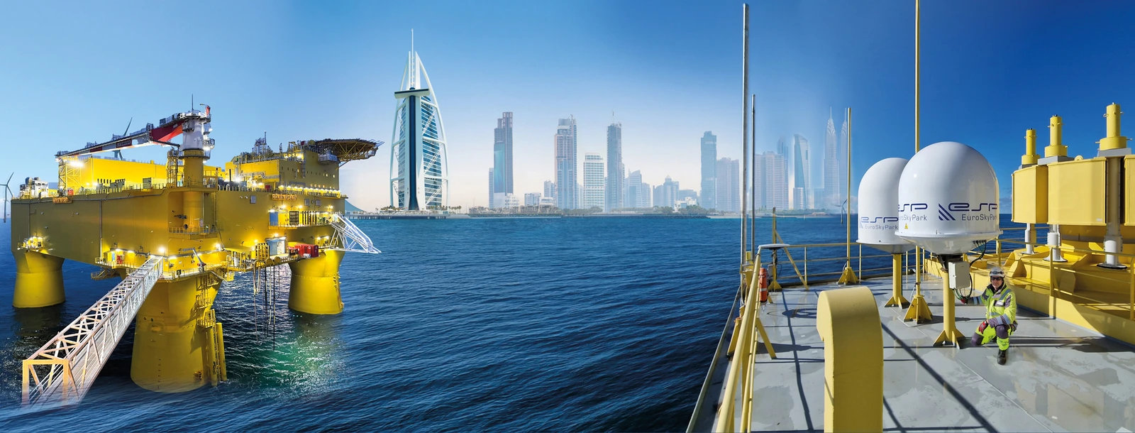 Composing aus 3 Elementen: Im Hintergrund Meer und am Horizont die Stadtsilhouette von Dubai. Links Offshore-Plattform in gelb. Rechts ESP-Antennen mit einem Mitarbeiter auf der Plattform.